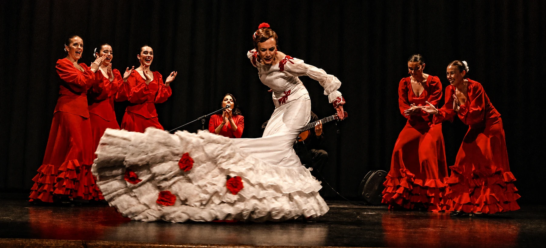 Elenco de Expresarte en una actuación de danza española, con bata de cola blanca y trajes rojos.