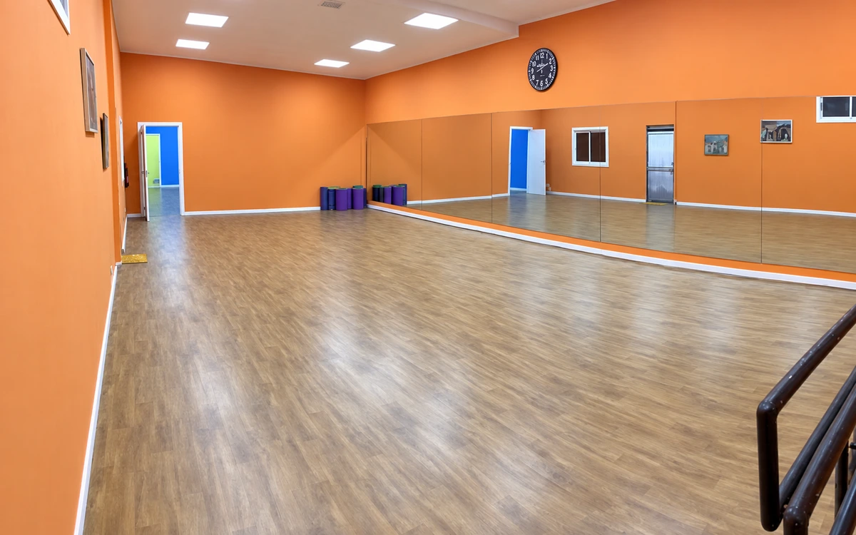 Sala Naranja: suelo de aspecto madera, pared de espejos y espacio de ensayo vacío